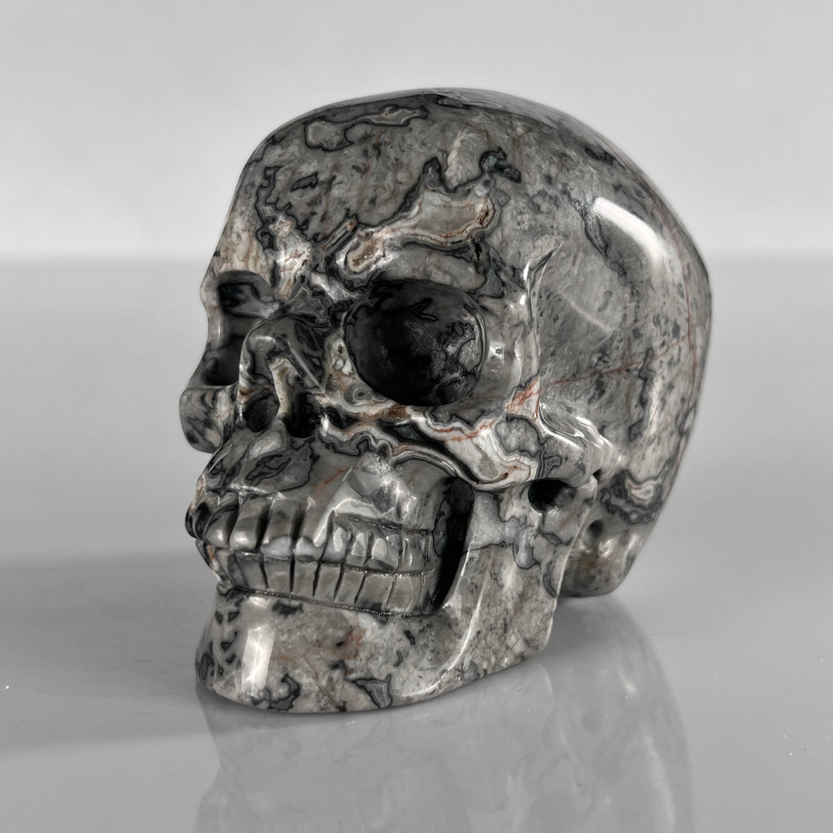 Left-front view of a 3-inch Grey Picture Jasper human skull carving