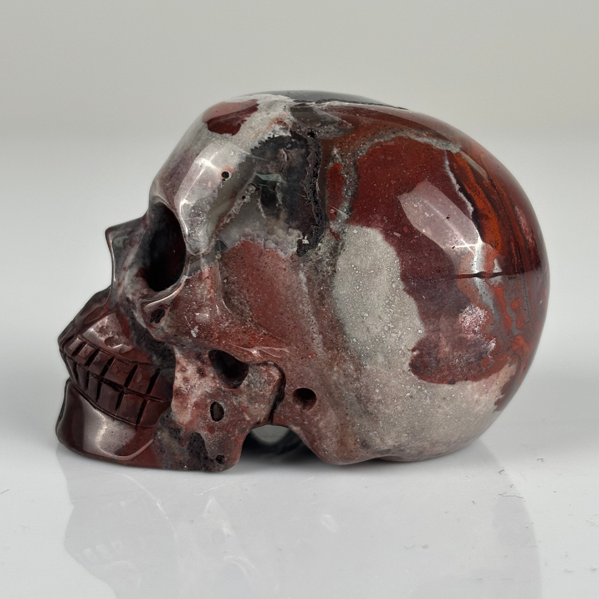 Left view of a 2-inch Red Crazy Lace Agate human skull carving