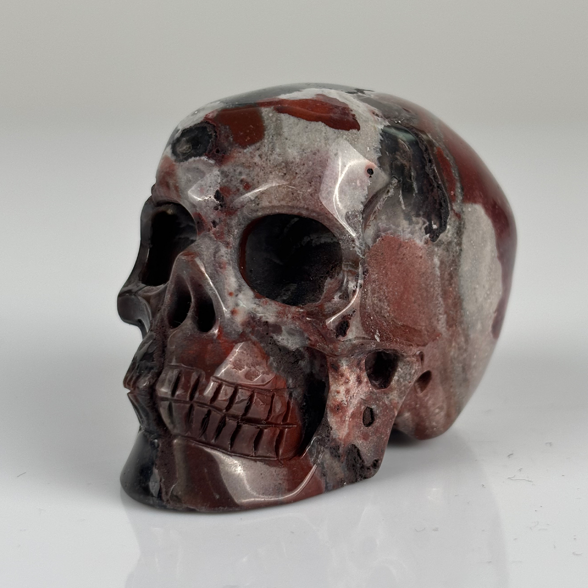 Left-front view of a 2-inch Red Crazy Lace Agate human skull carving